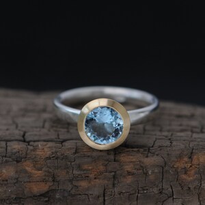 Puede incluir: Un anillo de plata con una piedra preciosa azul redonda engastada en un engaste de oro.