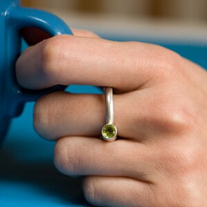 Pu&ograve; includere: Un anello d'argento con una pietra preziosa verde incastonata al centro. L'anello &egrave; indossato su un dito.