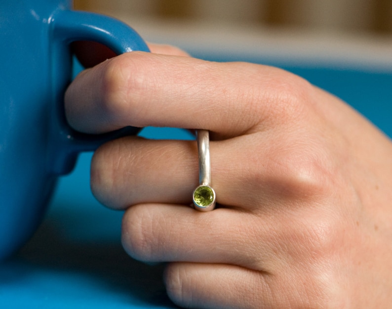 Pu&ograve; includere: Un anello d'argento con una pietra preziosa verde incastonata al centro. L'anello &egrave; indossato su un dito.