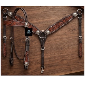 Op de afbeelding: Een donkerbruin lederen borsttuig voor paarden met gedetailleerd bloemmotief en een lichtbruine afwerking. Het item is voorzien van zilverkleurige metalen gespen, conchos en beslag, inclusief een zwart label met de tekst ALISH.