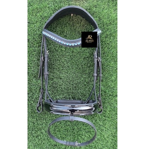 Puede incluir: Cabezada de caballo de cuero negro con acabado brillante. La testera está adornada con piedras preciosas azul claro. La cabezada incluye una muserola y una garganta. La marca "ALISH" es visible en un cuadrado negro.