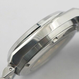May include: Close-up of a silver wristwatch with a metallic band. The watch case has a polished finish and a sleek, modern design. The watch band is made of interlocking metal links.