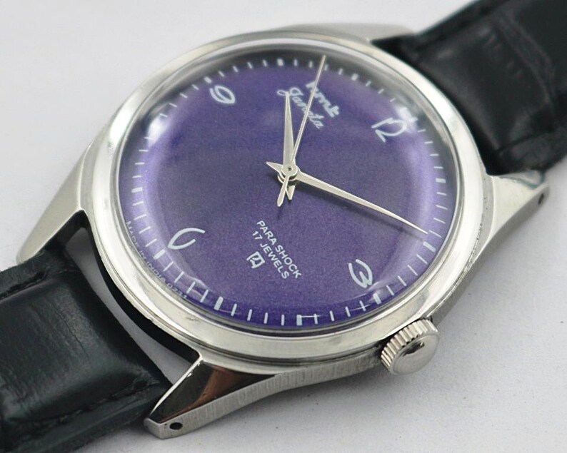 May include: A vintage wristwatch with a silver-toned case and a deep purple dial. The watch features silver hands and hour markers, with the text "Para Shock 17 Jewels". The watch has a black leather band.