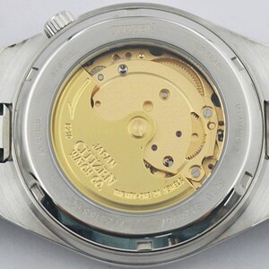 May include: Close-up of the back of a Citizen watch, showcasing the intricate internal mechanism. The watch has a silver-tone stainless steel band and case. The visible movement features gold-colored gears and a rotor, with text that reads "Citizen Watch Co."