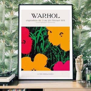 May include: A framed art print featuring a colorful floral design in red, yellow, and pink against a black and green background. The print includes the text "WARHOL" and exhibition details in French. The artwork is displayed in a black frame.