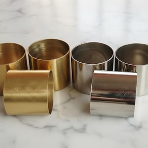 May include: A collection of six metal napkin rings in gold and silver. The napkin rings are cylindrical, with a simple, modern design. The gold rings have a brassy finish, while the silver rings are polished. Perfect for elegant table settings.