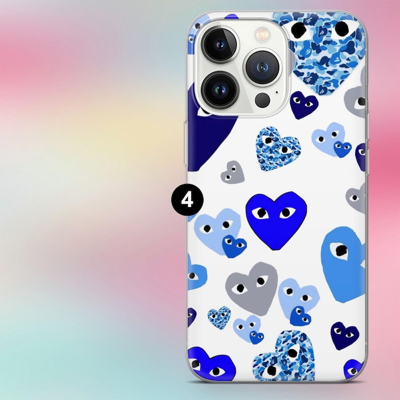 K&ouml;nnte beinhalten: Eine wei&szlig;e Handyh&uuml;lle mit einem sich wiederholenden Muster aus blauen Herzen. Die Herzen variieren in Gr&ouml;&szlig;e und Design, einige mit Augen, andere mit Camouflagemuster. Die H&uuml;lle hat einen transparenten Rand und einen dunkelblauen Akzent.