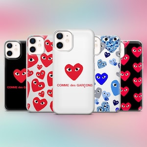 K&ouml;nnte beinhalten: Eine Auswahl an Handyh&uuml;llen mit Herzmotiven. Die H&uuml;llen zeigen ein rotes Herz mit Augen, einen wei&szlig;en Hintergrund und den Text "COMME des GAR&Ccedil;ONS". Andere H&uuml;llen haben Herzmuster in verschiedenen Farben.