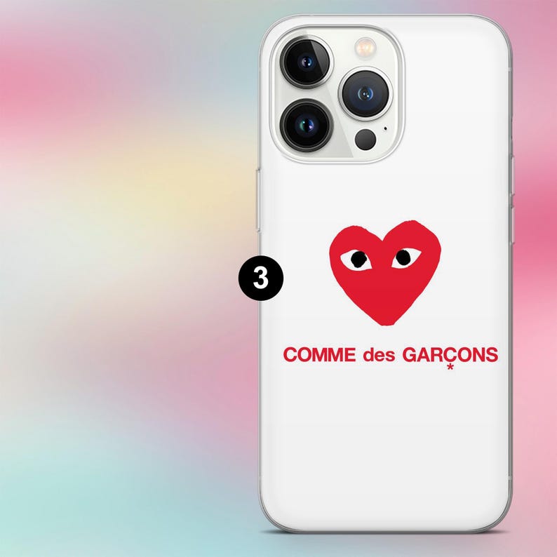 K&ouml;nnte beinhalten: Wei&szlig;es Handycase mit rotem Herz-Logo und dem Text "COMME des GAR&Ccedil;ONS". Das Case hat eine glatte Oberfl&auml;che und einen Kameraausschnitt.
