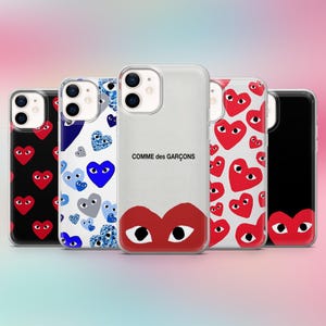 Puede incluir: Una colección de fundas para teléfonos con varios diseños. Una funda es transparente con el texto "COMME des GARÇONS" y un corazón rojo con ojos. Otras fundas presentan patrones de corazones rojos, azules y negros.