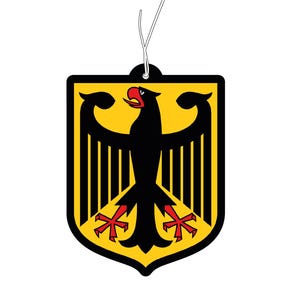 Könnte beinhalten: Ein schildförmiger hängender Lufterfrischer mit gelbem Hintergrund und einem schwarzen Adleremblem. Der Adler hat rote Krallen und einen roten Schnabel, das gesamte Motiv ist von einem dicken schwarzen Rand umgeben und oben mit einer weißen Schnur versehen.