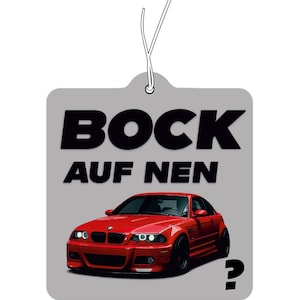 Könnte beinhalten: Ein grauer, quadratischer Lufterfrischer mit einer Grafik eines roten Sportwagens und dem schwarzen Text BOCK AUF NEN sowie einem Fragezeichen unten rechts. Der Artikel verfügt über eine weiße Schnur an der Oberseite zum Aufhängen.