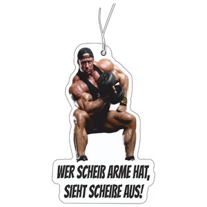 Könnte beinhalten: Ein hängender Lufterfrischer mit einer muskulösen Person in schwarzem Tanktop und Kappe, die eine dunkle Hantel hebt. Der Text unten lautet: WER SCHEIß ARME HAT, SIEHT SCHEIßE AUS! Das Design ist gestanzt mit weißem Rand und einer Aufhängeschnur.