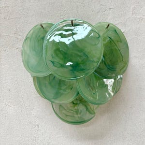 May include: A wall-mounted light fixture featuring multiple overlapping circular glass discs in varying shades of translucent green with a marbled effect. The discs are arranged in a cluster and attached to a central metal frame, creating a layered appearance.