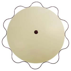 May include: Overhead view of a round, cream-colored table with a dark brown, wavy metal edge. A small, dark brown dot is centered on the table's surface. The table's design is simple and elegant.