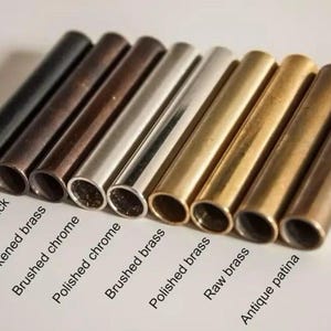 May include: An assortment of metal tubes in various finishes, including matte black, antique black, and brushed brass. The tubes are arranged in a row, showcasing different colors and textures. Text labels identify each finish.