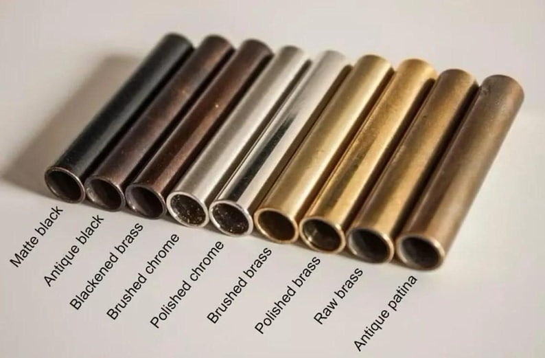 May include: An assortment of metal tubes in various finishes, including matte black, antique black, and brushed brass. The tubes are arranged in a row, showcasing different colors and textures. Text labels identify each finish.