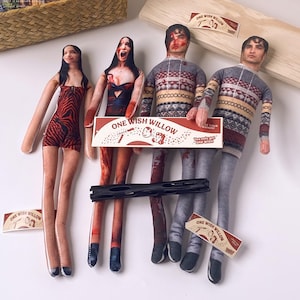 Puede incluir: Cuatro muñecos de tela personalizados con rostros y ropa impresos. Dos muñecos llevan jerséis estampados, uno lleva un vestido con estampado de tigre rojo y negro, y otro lleva un vestido negro con detalles rojos. Incluye caja ONE WISH WILLOW.