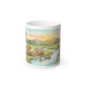 Könnte beinhalten: Weißer Keramikbecher mit einer Aquarellillustration von Wasserschweinen und Faultieren in der Nähe eines Flusses bei Sonnenuntergang. Das Design umfasst eine Landschaft mit Bergen, Palmen und einem farbenfrohen Himmel. Der Becher hat eine Standardgröße.