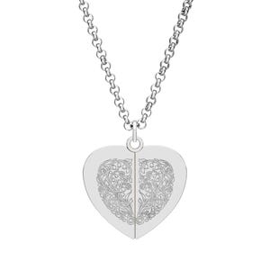 Könnte beinhalten: Eine silberfarbene Halskette mit einem herzförmigen Anhänger. Der Anhänger ist zweigeteilt und mit einem eingravierten floralen Design versehen. Die Kette ist im filigranen Glieder-Stil gehalten, und der Anhänger hängt an einer kleinen Schlaufe.