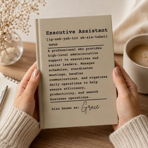 Op de afbeelding: Een lichtbeige notitieboek met zwarte tekst met een woordenboekdefinitie van Executive Assistant, inclusief fonetische spelling, een gedetailleerde functiebeschrijving en de handgeschreven tekst Also known as: Grace.