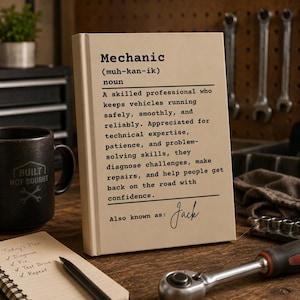 以下が含まれることがあります： Mechanicという単語の辞書風の定義が書かれた長方形のベージュ色の看板。発音記号、職業に関する説明文、そして黒い筆記体フォントでAlso known as: Jackというテキストが記載されています。