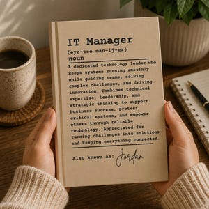 Può includere: Un libro con copertina rigida beige che presenta una definizione in stile dizionario di IT Manager stampata in nero. La copertina include una pronuncia fonetica, un paragrafo descrittivo sul ruolo e il nome scritto a mano Jordan in basso.