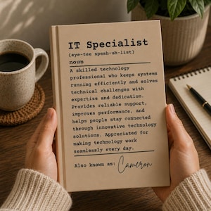 May include: A beige notebook with black text featuring a dictionary-style definition of an IT Specialist, describing a skilled technology professional who solves technical challenges, with the handwritten name Cameron at the bottom.