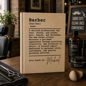 Op de afbeelding: Een beige boek met zwarte tekst met de definitie van een barbier, inclusief de tekst "Barber (bar-ber) noun" gevolgd door een beschrijvende alinea en de gepersonaliseerde tekst "Also known as: Michael" in een cursief lettertype.