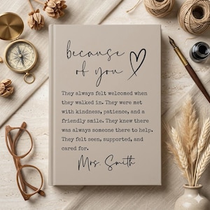 May include: A beige journal with the words "because of you" and a heart symbol. The journal has text about feeling welcomed and supported, signed "Mrs. Smith". A compass, glasses, and writing supplies are arranged around the journal.