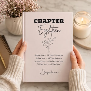 Pode incluir: Um diário de capa dura rosa claro com as palavras "CHAPTER Eighteen" em preto. Abaixo do título, há uma ilustração floral e o texto "Behind You - All Your Memories, Before You - All Your Dreams, Around You - All Who Love You, Within You - All You Need, Sophia."