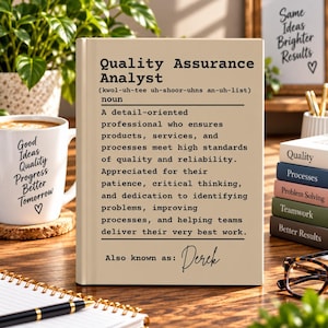 May include: A beige rectangular sign featuring the black printed definition of a Quality Assurance Analyst, including phonetic pronunciation and a description of professional duties, with the text Also known as: Derek at the bottom.