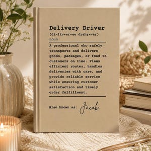 Op de afbeelding: Een beige hardcover boek met een woordenboekachtige definitie van de term Delivery Driver in zwarte tekst. Het item bevat een fonetische spelling, een classificatie als zelfstandig naamwoord, een functiebeschrijving en de naam Jacob.