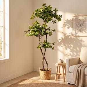 Op de afbeelding: Een hoge, kunstmatige boom met twee in elkaar verstrengelde bruine stammen en levendige groene, ronde bladeren. De boom staat in een ronde, lichtgekleurde mand van gevlochten riet met twee handvatten, geplaatst op een getextureerde vloer.