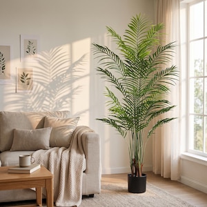 Puede incluir: Una palmera artificial alta con frondas plumosas de color verde vibrante que se extienden desde tallos delgados y erguidos. La planta está colocada en una maceta cilíndrica negra sencilla, sobre una superficie de suelo texturizada cerca de una ventana.