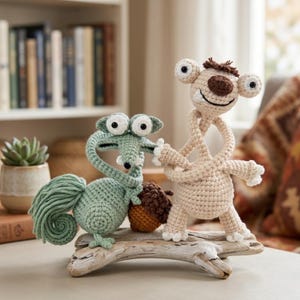 Könnte beinhalten: Gehäkelte Figuren eines Eichhörnchens und eines Faultiers, inspiriert von dem Animationsfilm "Ice Age". Das Eichhörnchen ist grün mit einem langen Schwanz, und das Faultier ist beige. Sie stehen auf einem Stück Treibholz, mit einer Eichel dazwischen.