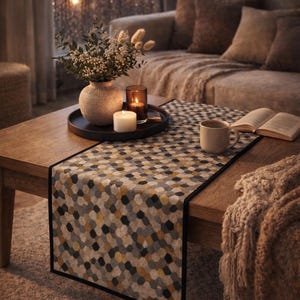 Peut inclure: Un chemin de table rectangulaire présentant un motif géométrique répétitif d'hexagones dans des tons de gris, jaune moutarde et blanc. Le chemin de table possède une bordure noire unie et est posé sur une table basse en bois texturé.