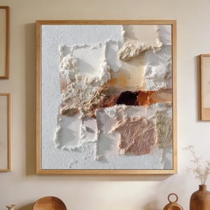 Puede incluir: Arte mural abstracto texturizado en un marco de madera cuadrado. La obra presenta una composición en capas de bloques texturizados blancos, beige, marrones y rosas. La pieza tiene una estética moderna y minimalista, adecuada para la decoración del hogar.