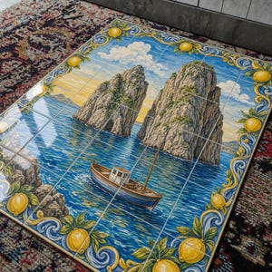 May include: A rectangular wall art piece composed of twelve ceramic tiles featuring a painted scene of a small boat on blue water near two large rocky cliffs. The border is decorated with yellow lemons and green leaves on a blue scroll background.