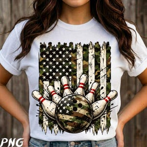 May include: A white short-sleeved t-shirt featuring a graphic print of a distressed American flag in camouflage colors. The design includes five white bowling pins with red stripes and a bowling ball with a camouflage and star pattern.