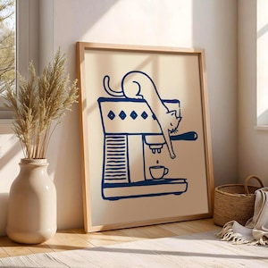 May include: A framed art print shows a navy blue illustration of a cat and an espresso machine. The cat is on top of the machine, reaching down towards a cup. The print has a light beige background and a wooden frame.