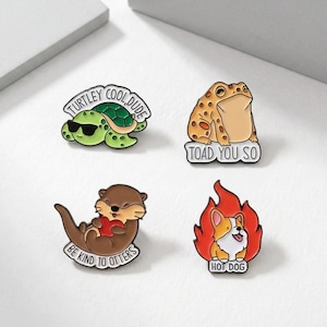 Pode incluir: Quatro pins de esmalte com desenhos de animais. Uma tartaruga verde usando óculos de sol com o texto "TURTLEY COOL DUDE". Um sapo castanho com o texto "TOAD YOU SO". Uma lontra marrom segurando um coração vermelho com o texto "BE KIND TO OTTERS". Um corgi em chamas com o texto "HOT DOG".