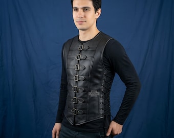 Könnte beinhalten: Eine schwarze Lederweste mit einem Vorderteil aus sieben horizontalen Riemen, die mit Metallschnallen befestigt sind. Die Seiten der Weste verfügen über eine Schnürung mit schwarzer Kordel. Der Text Elite Leather Attire ist auf der Brust sichtbar.