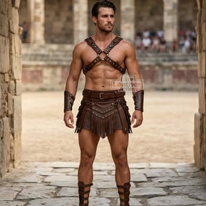 Könnte beinhalten: Ein braunes Leder-Harnisch im Gladiatorenstil, ein Gürtel mit Fransenrock und passende Armstulpen. Das Set ist mit Metallnieten und Schnallen versehen. Der Text Elite Leather Attire ist auf der Brust sichtbar. Enthält zudem Beinschützer.