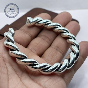 Può includere: Un braccialetto argentato con un design a corda intrecciata. Il braccialetto è realizzato in metallo lucido e ha un aspetto spesso e intrecciato. Il logo Royal Spark è visibile nell'angolo in alto a sinistra.