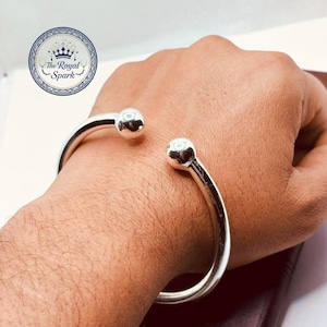 May include: A silver cuff bracelet with rounded ball ends. The open design allows for easy wear. The Royal Spark logo is visible in the background.