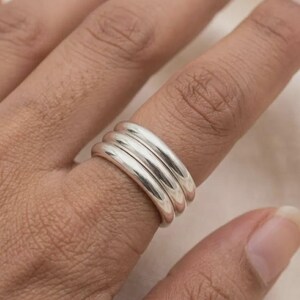 May include: A set of three smooth, polished silver bands worn together on a finger. The rings feature a rounded, minimalist profile with a reflective metallic finish, creating a stacked appearance that sits evenly across the finger joint.