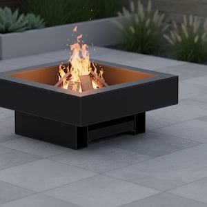 以下が含まれることがあります： 暖炉のあるモダンな正方形の黒いファイヤーピット。内側は温かみのあるオレンジ色です。炎と燃える木がピットの中にあります。ファイヤーピットは灰色のタイルのパティオに設置され、背景には緑があります。