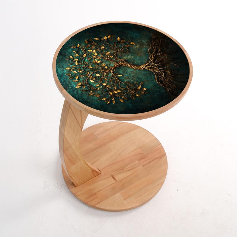 May include: A wooden side table with a round top featuring a teal and gold tree design. The tree's branches and leaves are gold against a teal background. The table has a curved leg and a circular base, all made of light-colored wood.