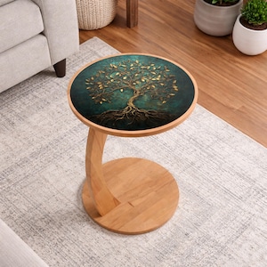 Pode incluir: Uma mesa lateral redonda com base de madeira e um design de árvore da vida verde e dourado no tampo. A mesa tem uma perna curva e uma base circular. O tampo da mesa tem aproximadamente 46 cm de diâmetro.